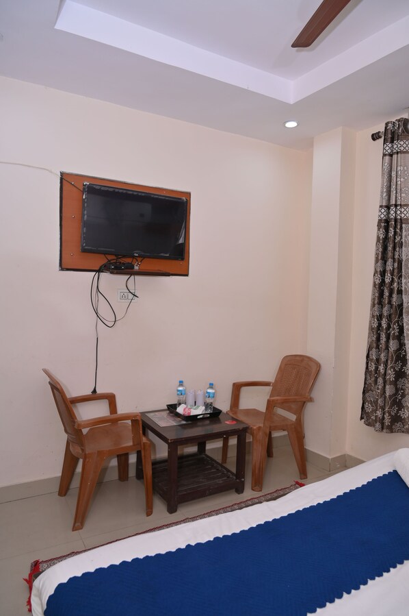 Habitación de hotel con cama, televisor montado en la pared, una mesita con dos sillas y ventana con cortinas.