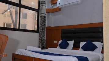Un dormitorio con cama, ventilador de techo, equipo de aire acondicionado, ventana y alfombra estampada.