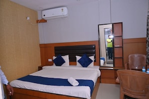 Una habitación de hotel con cama, mesita de noche, silla, aire acondicionado y espejo.
