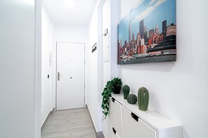 A hallway with a white door, a cityscape painting, and a plant on a white console. - Studio in Nerja Near Torrecilla Beach (Nerja)