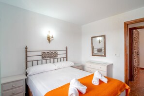 A hotel room with a bed, a nightstand, a dresser, a mirror, and an open door leading to another room. - Holiday Home in Nerja With Sea Views (Nerja)