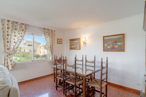 A dining area with a table and chairs, a window with curtains, and two framed pictures on the wall. - Holiday Home in Nerja With Sea Views (Nerja)