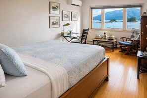 A bedroom with a bed, a desk, a chair, and a window with a view of mountains and water. - Oceanfront Home w/ Private Dock & Beach (Ketchikan)