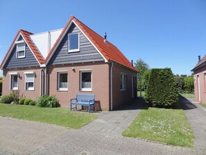 A two-story house with a red roof, a blue bench in front, and a well-maintained lawn. - Holiday Home With 2 Bedrooms (Oostkapelle)