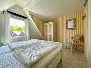A bedroom with a bed, a chair, a wardrobe, and a window with curtains. - Holiday Home With 2 Bedrooms (Oostkapelle)