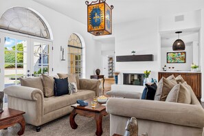 A spacious living room with a fireplace, a large arched window, and a hanging lantern. - Private Pool + Hot Tub + Fire Pit + Covered Patio | Mins to Golf | Casa Talavera (Scottsdale)