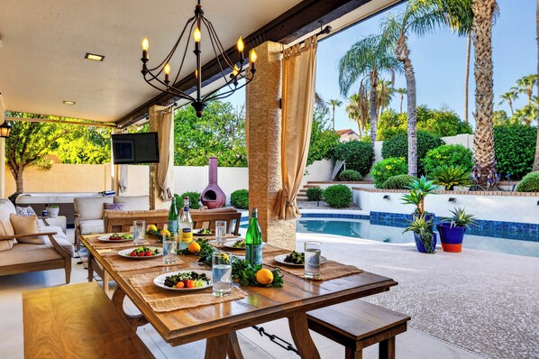 Un área de comedor al aire libre con piscina y palmeras.