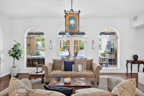 A spacious living room with a sofa, coffee table, and a large window with a view of a pool and outdoor furniture. - Private Pool + Hot Tub + Fire Pit + Covered Patio | Mins to Golf | Casa Talavera (Scottsdale)