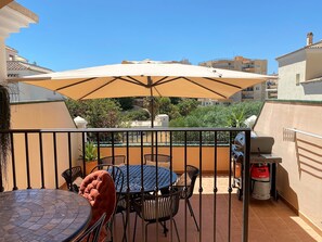 A terrace with a round table and chairs, a large umbrella, and a barbecue grill. - Villa in Nerja Near Burriana Beach (Nerja)