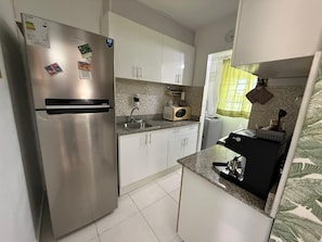 Eine kompakte Küche mit Edelstahlkühlschrank, weißen Schränken, einer Mikrowelle und einem Spülbecken.