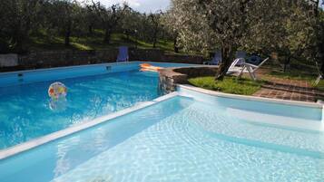 Une piscine rectangulaire à l’eau d’un bleu cristallin, entourée d’un mur de pierre et d’arbres.