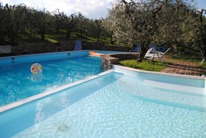 Une piscine rectangulaire à l’eau d’un bleu cristallin, entourée d’un mur de pierre et d’arbres.