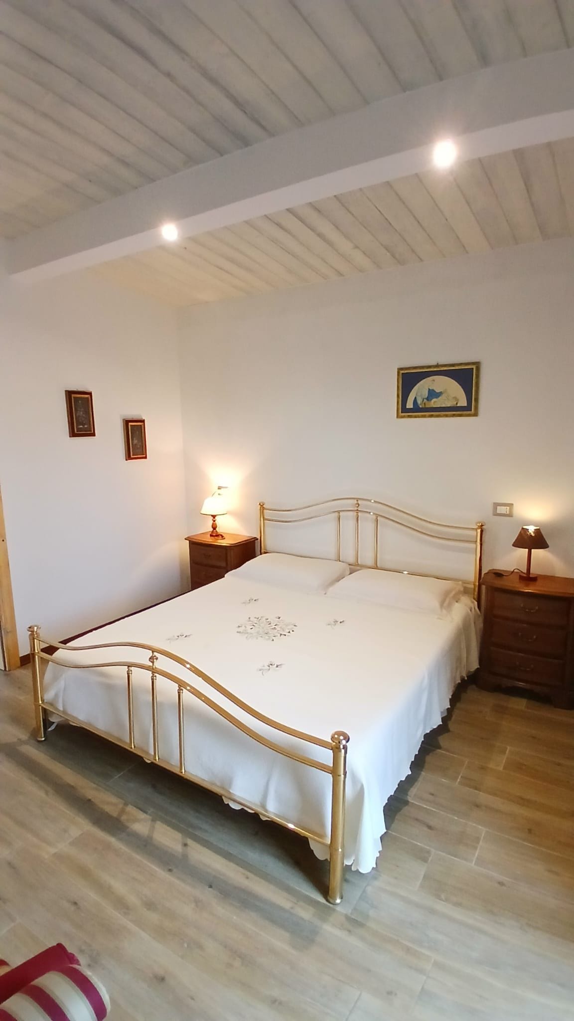 Une chambre à coucher avec un lit, deux tables de chevet, un tableau accroché au mur et un plancher en bois.