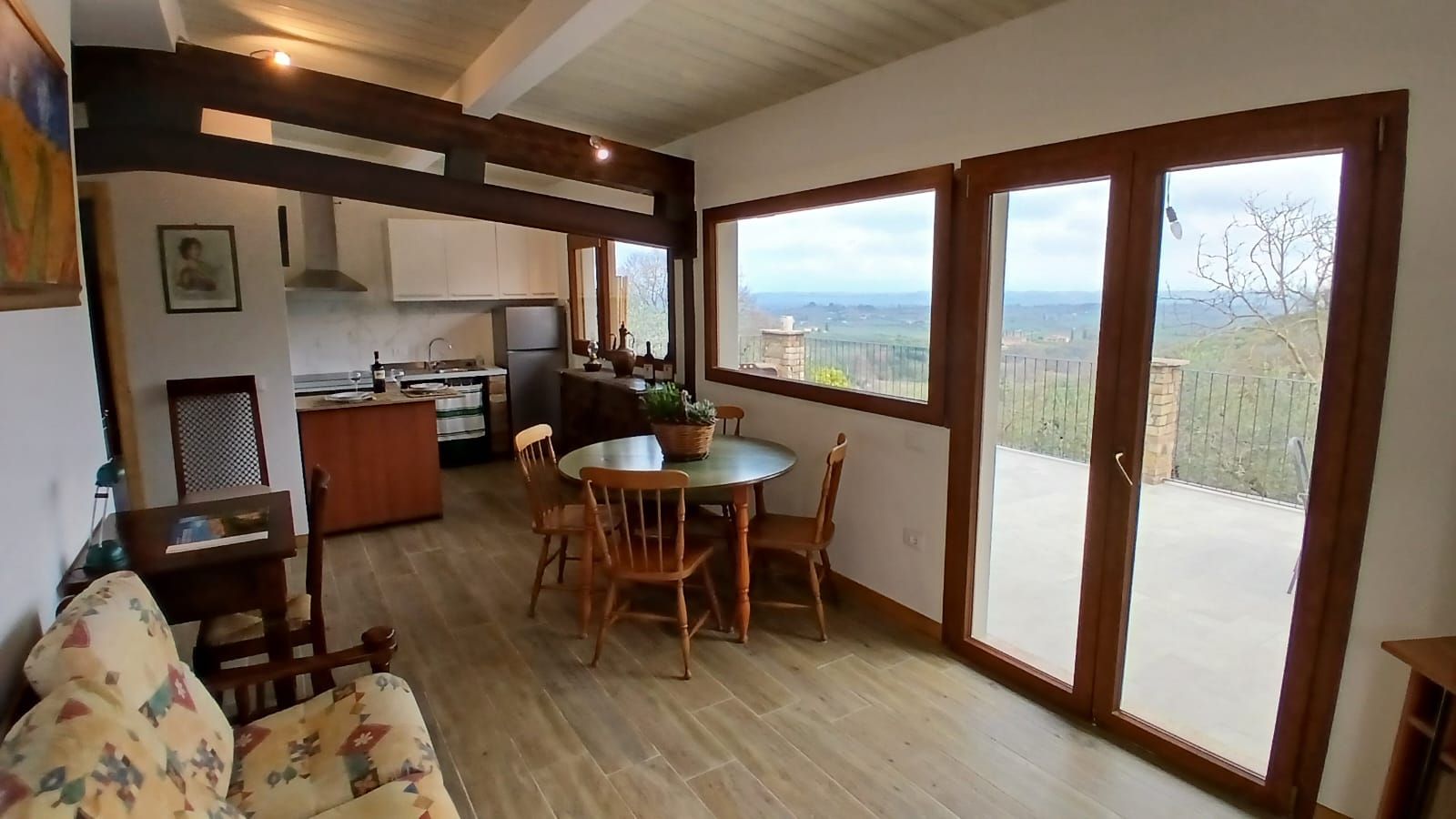 Un vaste espace de vie comprenant un coin repas avec table et chaises, une cuisine avec des meubles blancs et une grande porte-fenêtre coulissante donnant sur une terrasse extérieure.