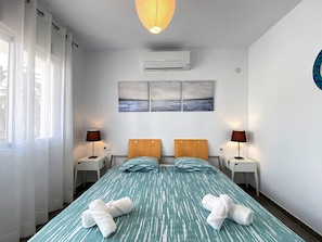 A hotel room with a bed, two bedside tables, lamps, an air conditioning unit, and artwork on the wall. - Holiday Home in Nerja Near Playa Carabeillo (Nerja)