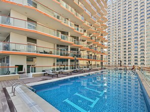 Ein modernes Hotel mit einem Rooftop-Infinity-Pool, mehreren Balkonen und einem Hochhaus im Hintergrund.