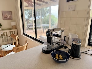 A kitchen with a coffee maker, a bowl of coffee cups, and a window with a view of the outdoors.