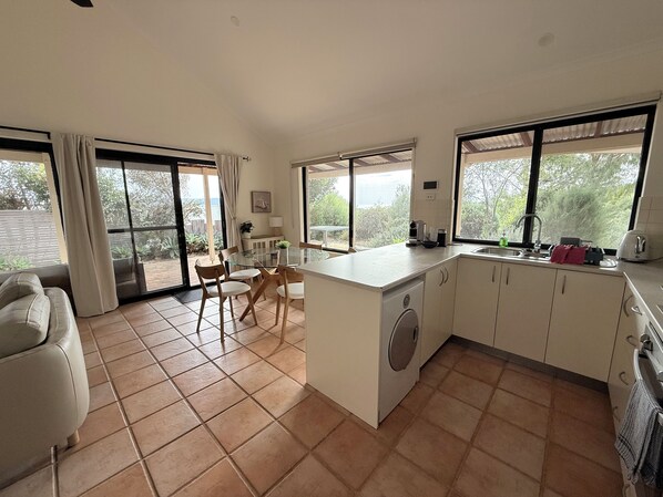 A compact kitchen with a dining area, large windows, and a washing machine.