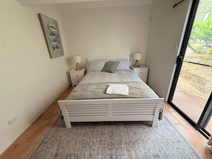 A bedroom with a bed, two bedside tables, a nightstand, a window with a view, and a wall-mounted picture.