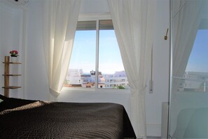 A bedroom with a bed, a window with curtains, a view of buildings, and a wooden ladder. - Villa in Nerja Near Burriana Beach & Pool (Nerja)