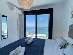 A hotel room with a large bed, a view of the sea, and a balcony with outdoor furniture. - Duplex in Nerja With Stunning Sea Views (Nerja)