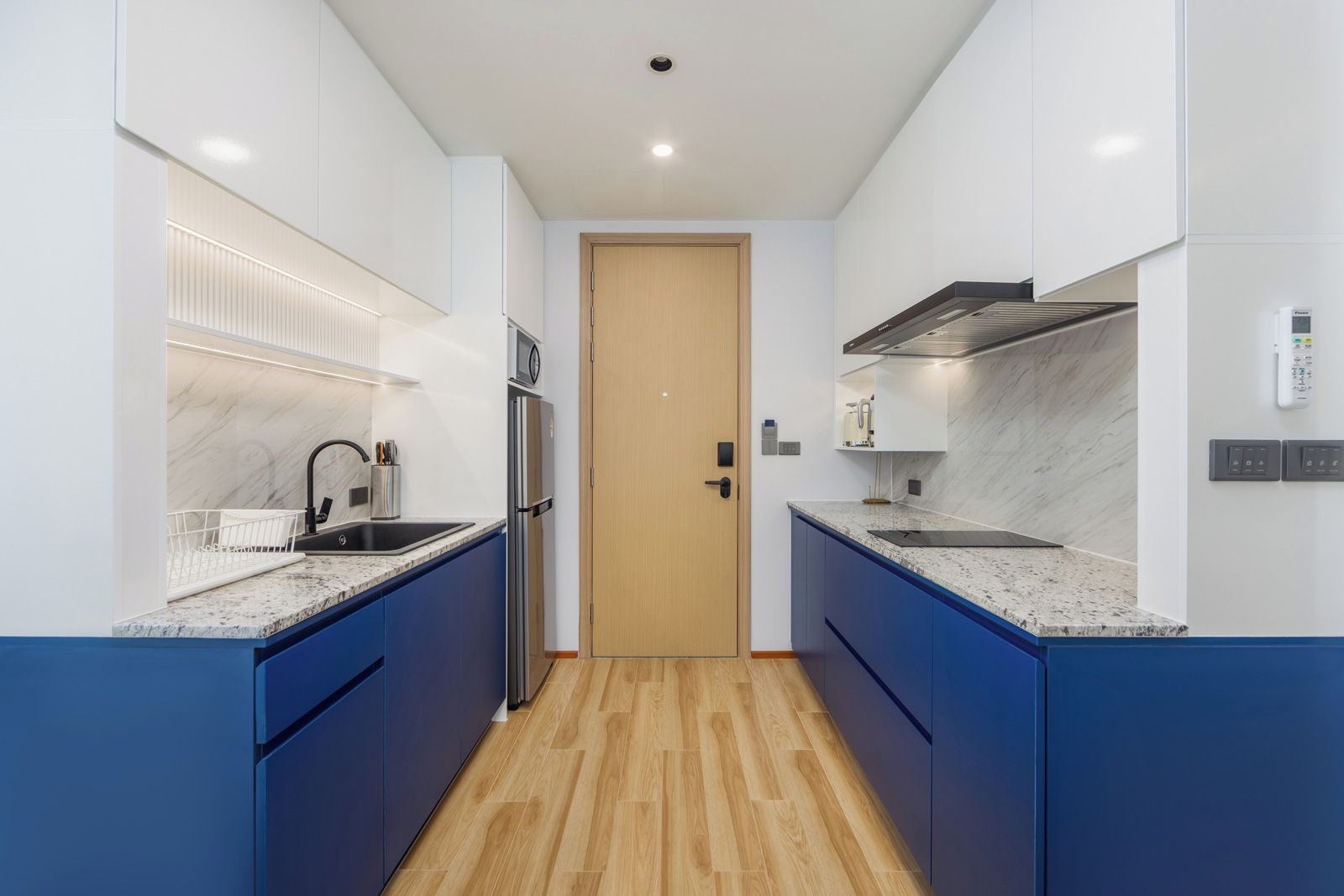 A modern kitchen with blue cabinets, a stainless steel refrigerator, and a wooden door.
