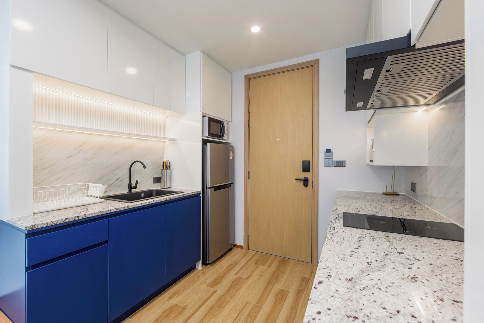 Una cocina moderna con microondas integrado, refrigerador de acero inoxidable y puerta de madera.
