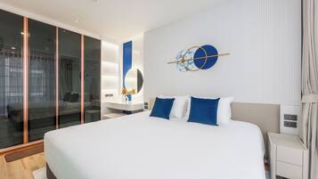 Une chambre d’hôtel moderne avec un grand lit, une cloison en verre, une table de chevet et une horloge fixée au mur.