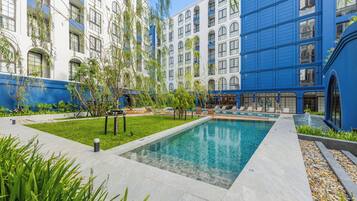 Un patio de hotel con piscina, sillas de descanso y un edificio azul con ventanas arqueadas.