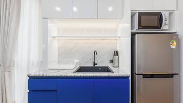 Una cocina con un refrigerador de acero inoxidable, un microondas, un lavamanos con grifo y armarios azules.