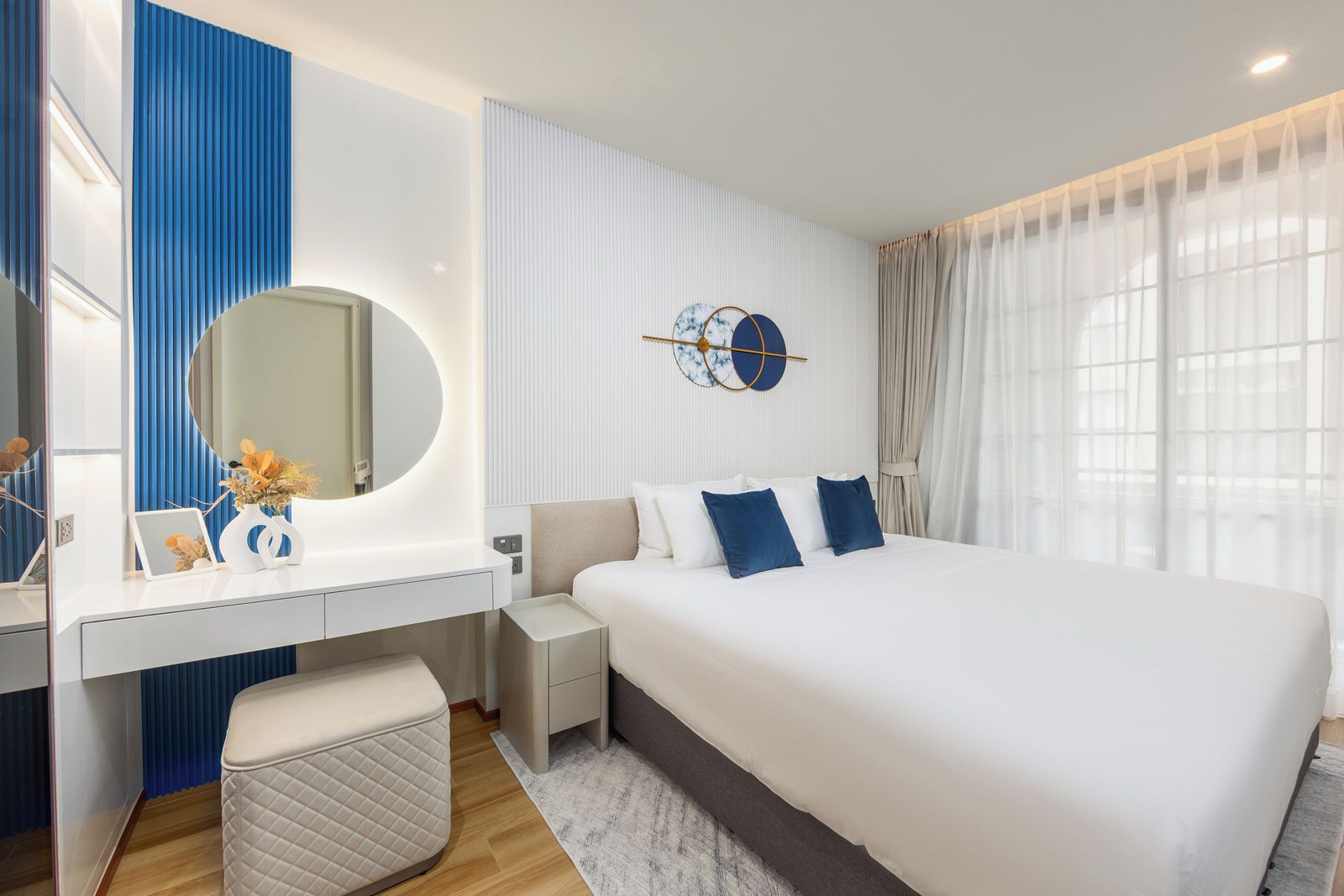 A modern hotel room with a large bed, a bedside table, a mirror, and a wall-mounted clock.