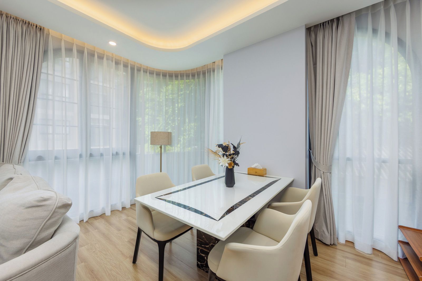 Un espace repas moderne avec une table en marbre, des chaises de couleur beige et des rideaux légers.