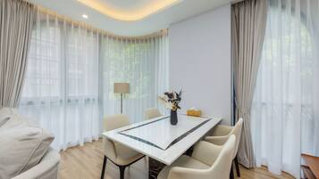 Un comedor moderno con una mesa de mármol, sillas color beige y cortinas de gasa.