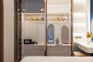Habitació d'hotel amb un vestidor que conté roba penjada, una taula de planxar i una caixa forta.