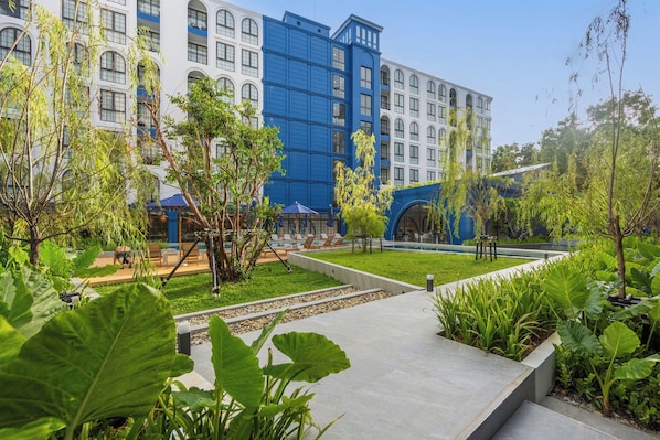 A hotel courtyard with a pool, lounge chairs, and a variety of plants.