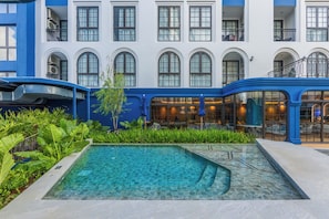 A hotel courtyard with a swimming pool, lush greenery, and a blue and white building facade.