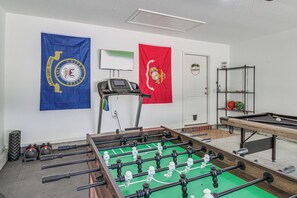 Ein Zimmer mit einem Kicker, einem Laufband und zwei Wimpeln an der Wand.