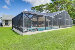 A covered outdoor pool area with a glass enclosure, a lawn, and a house in the background. - Private Pool! Family Escape, 11 Mi to Jensen Beach (Port St. Lucie)