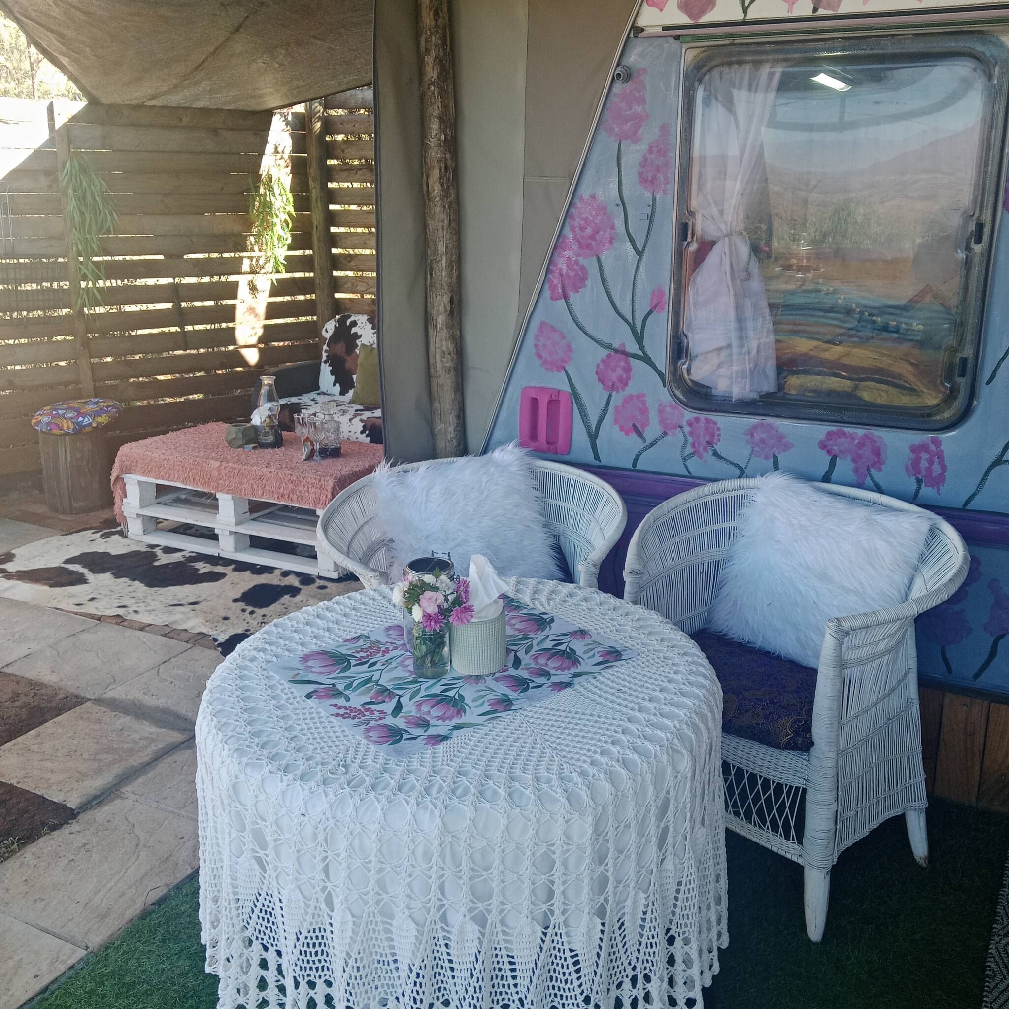 Un espace extérieur accueillant, aménagé avec une table ronde, deux chaises en osier blanches et une nappe décorative.