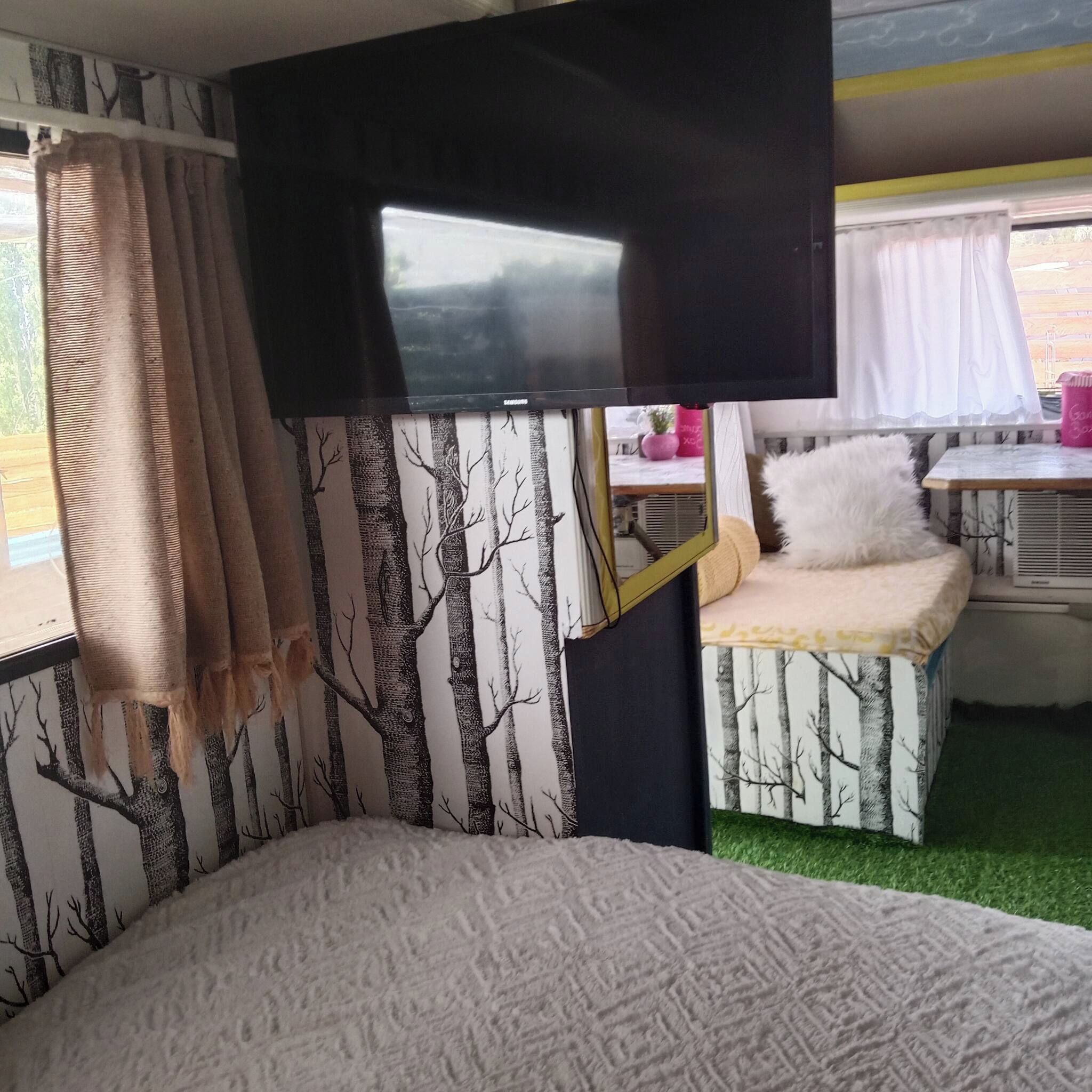 Un intérieur chaleureux avec un lit, un téléviseur à écran plat et une petite table agrémentée d’un coussin.