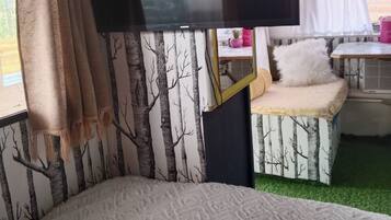 Un intérieur chaleureux avec un lit, un téléviseur à écran plat et une petite table agrémentée d’un coussin.