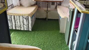 A compact living space with a green artificial grass floor, a small table with a pink object, and a sofa with a tree pattern.