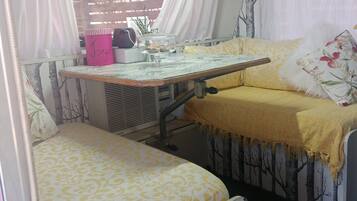 A compact living space with a bed, a small table with a glass top, and a chair.