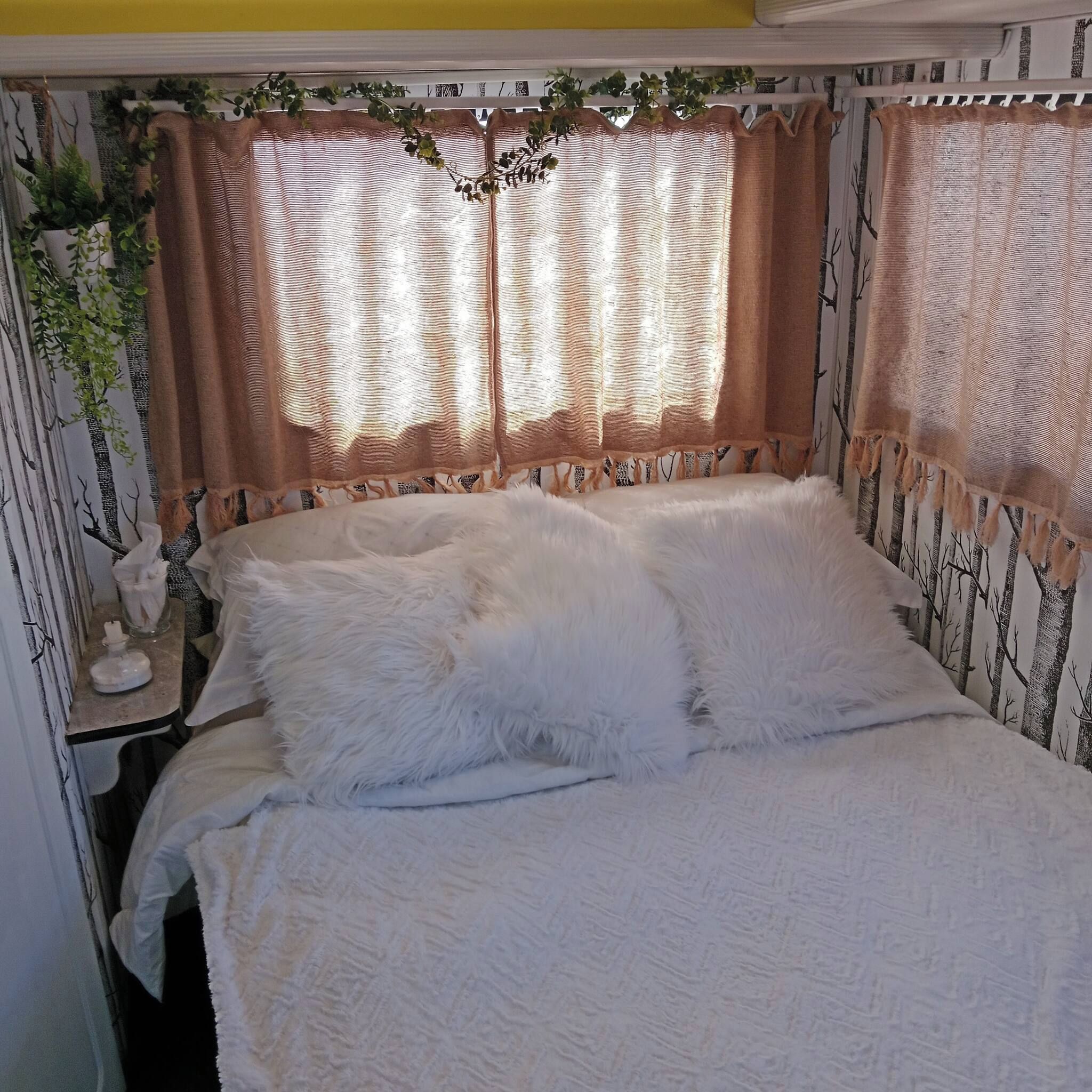 A bed with white bedding, a nightstand with a lamp, and a wall with a tree pattern.