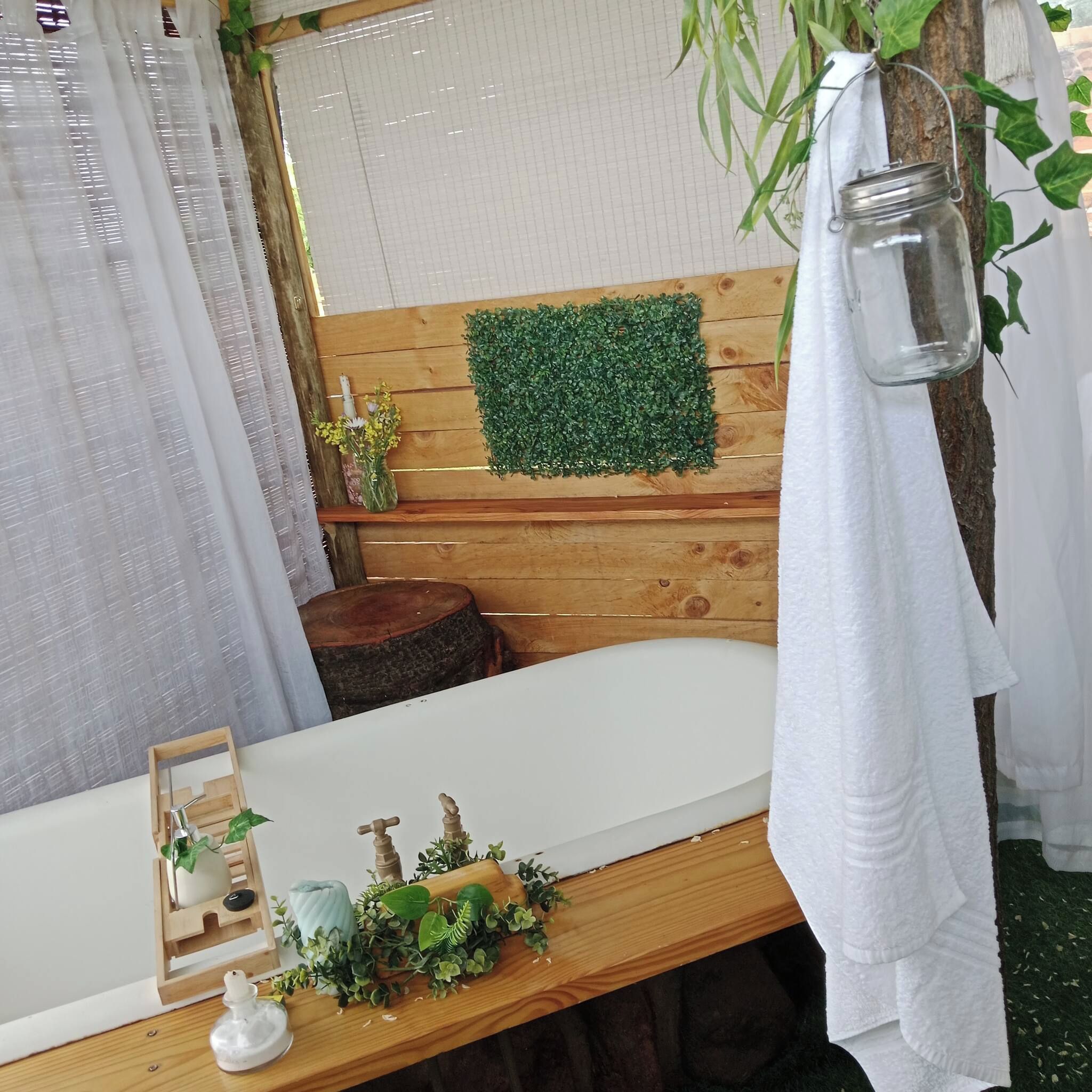 Une salle de bain avec un meuble-lavabo en bois, un miroir, un mur recouvert de gazon artificiel vert, une lanterne suspendue et une petite plante posée sur le meuble-lavabo.