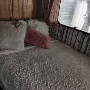 A bed with patterned bedding, a window with curtains, and a wall with a tree pattern.