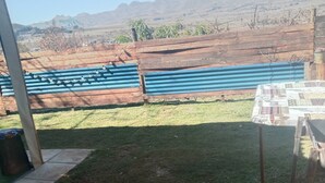 A backyard with a fire pit, a table with a patterned tablecloth, and a blue fence. - Romantic Clarens Getaway - Glamped Caravan with Braai & Fairy Bath (Clarens)