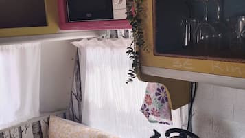 A compact kitchen with a microwave, a kettle, and a shelf with dishes.