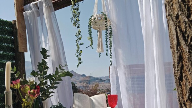 A rustic outdoor setting with a white bathtub, a wooden table with a red glass, and a hanging macrame decoration. - Romantic Clarens Getaway - Glamped Caravan with Braai & Fairy Bath (Clarens)
