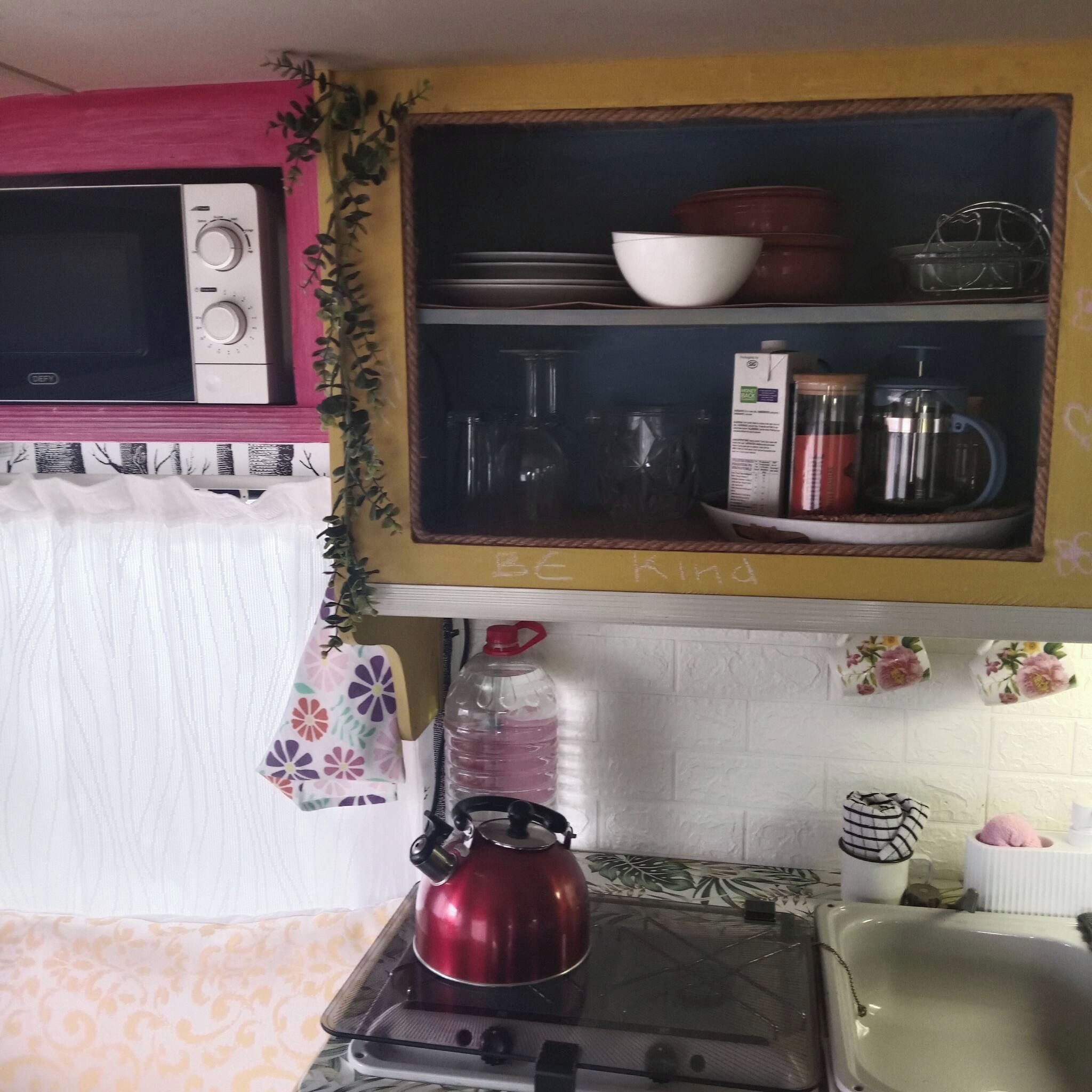 Una cocina con microondas, hervidor y diversos utensilios de cocina en estantes.